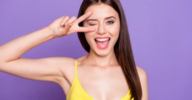 Close up portrait of beautiful dreamy attractive pretty gorgeous charming lovely lady in her yellow top make toothy smile she show v-sign near wink eye isolated on shine purple background