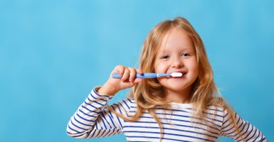A little girl in striped pajamas is brushing her teeth with a toothbrush. The concept of daily hygiene. On a blue background